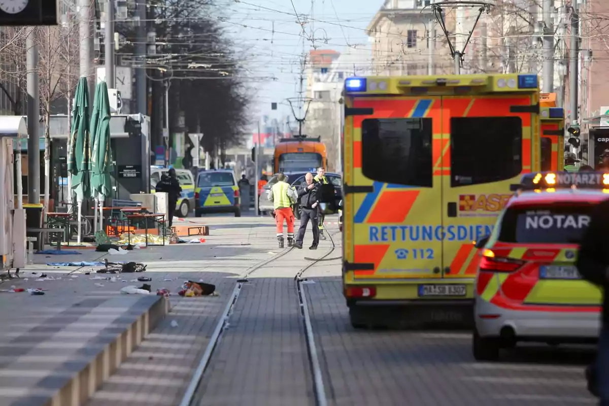 Una calle con vehículos de emergencia, incluyendo ambulancias y coches de policía, con personas trabajando en la escena.