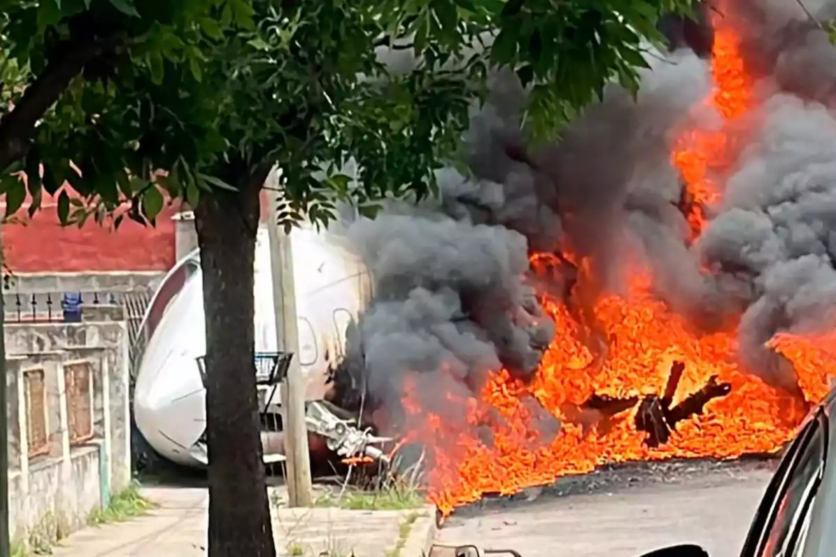 Un avión se estrella en una zona urbana y se incendia, generando llamas intensas y humo negro.