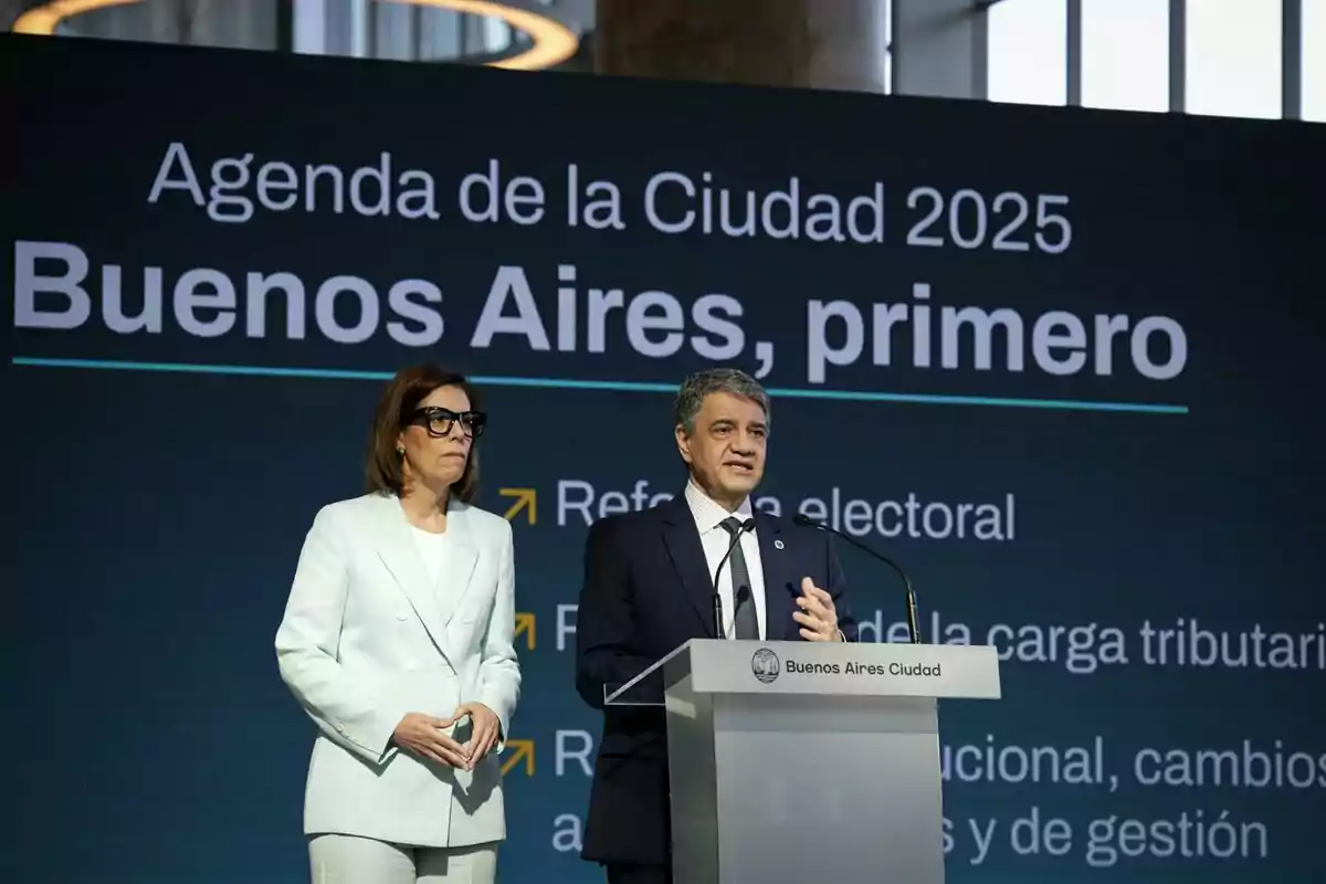 Dos personas en un escenario frente a un podio con un cartel que dice "Agenda de la Ciudad 2025 Buenos Aires, primero".