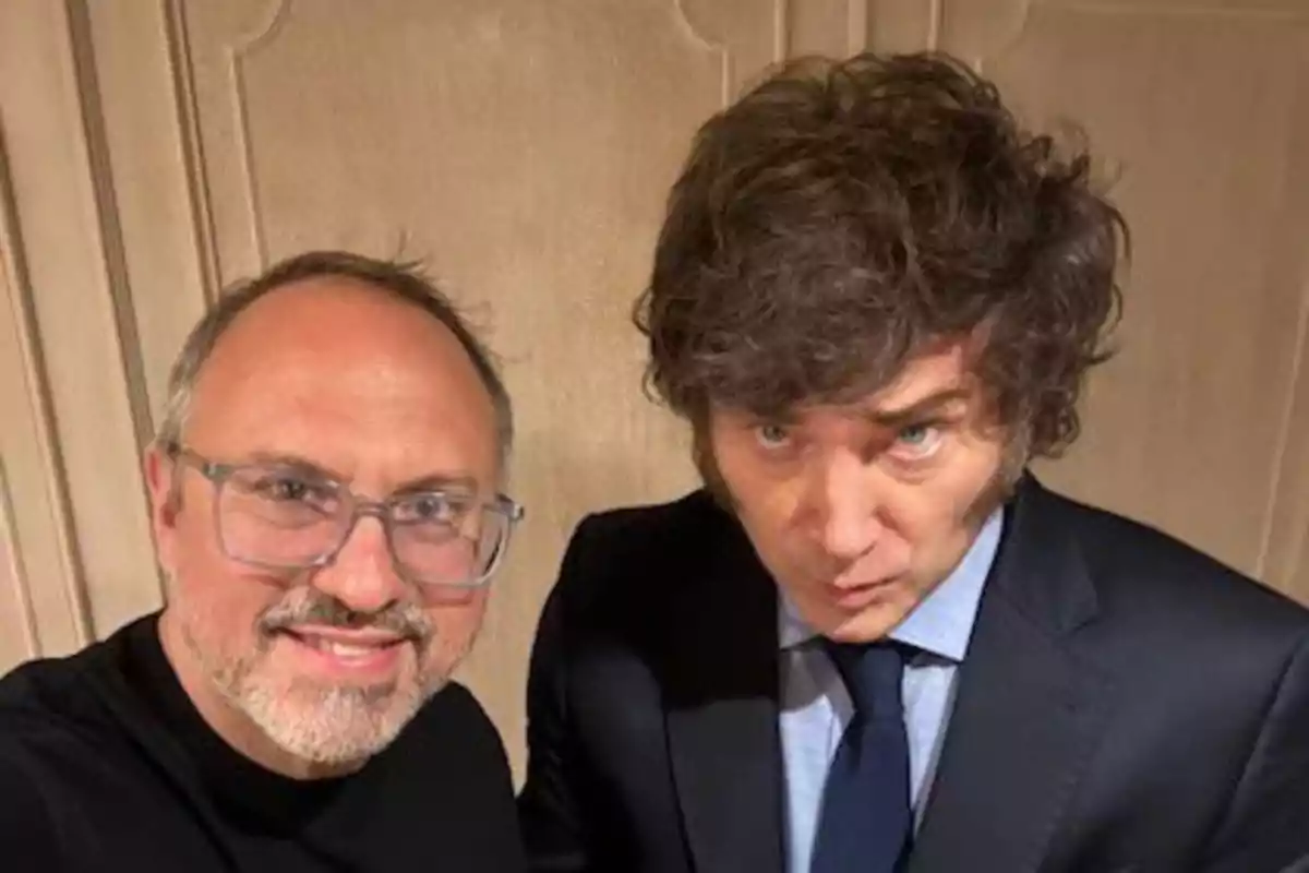 Dos hombres posando para una foto, uno con gafas y barba y el otro con cabello rizado y traje.