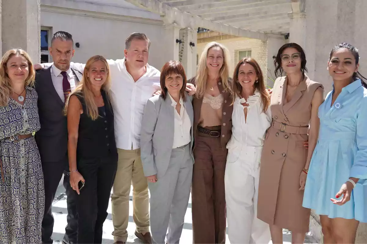 Un grupo de personas posando juntas al aire libre, algunas de ellas con ropa formal y otras con atuendos más casuales, en un entorno soleado con columnas de fondo.