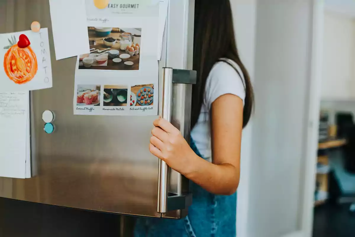 Una persona abriendo la puerta de un refrigerador con notas y recetas pegadas en la superficie.