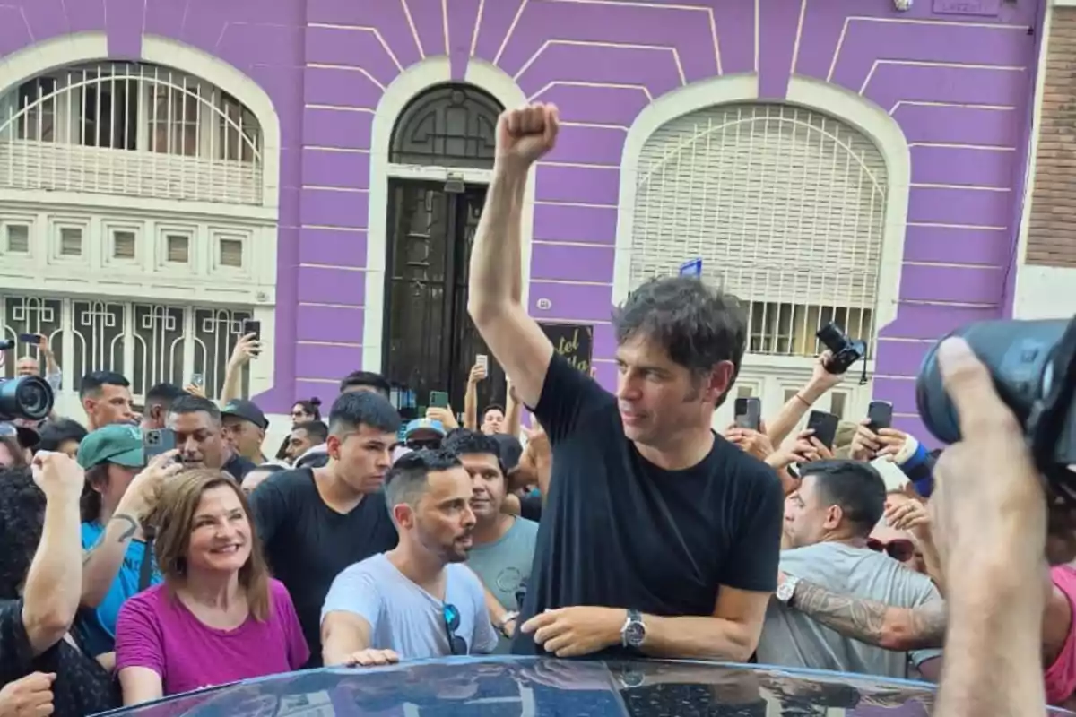 Un hombre levanta el puño mientras está rodeado de una multitud frente a un edificio de fachada morada.