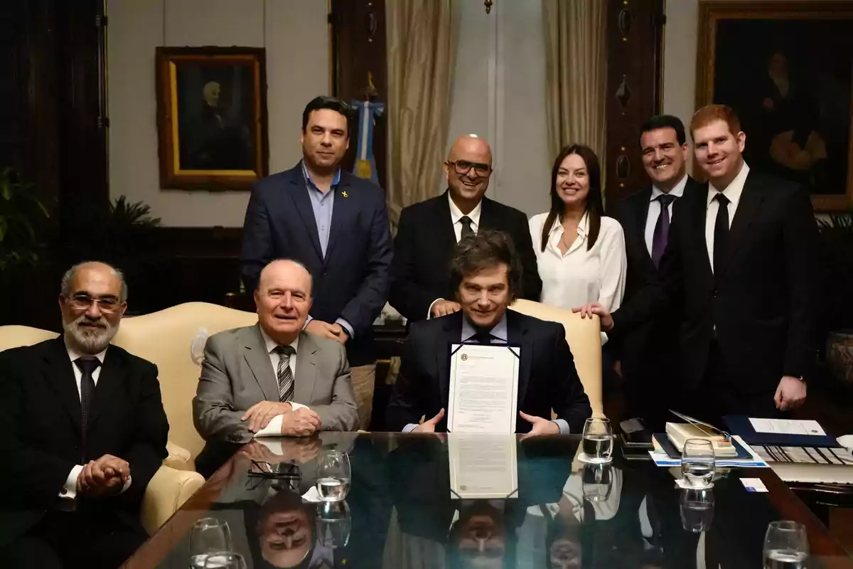 Un grupo de personas vestidas formalmente posando alrededor de una mesa en una oficina elegante, con una persona en el centro sosteniendo un documento.