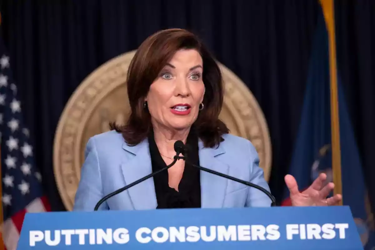 Woman speaking at a press conference with a sign that says 