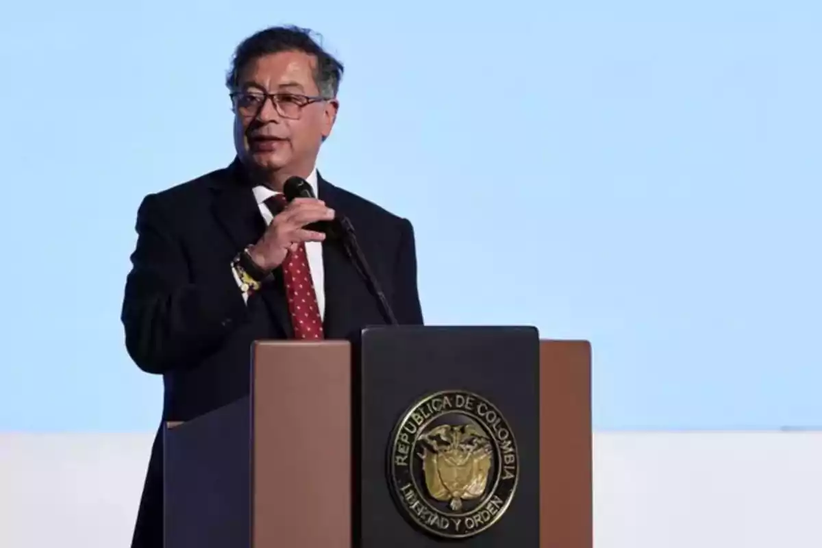 Un hombre en traje oscuro y corbata roja habla en un podio con el escudo de la República de Colombia.