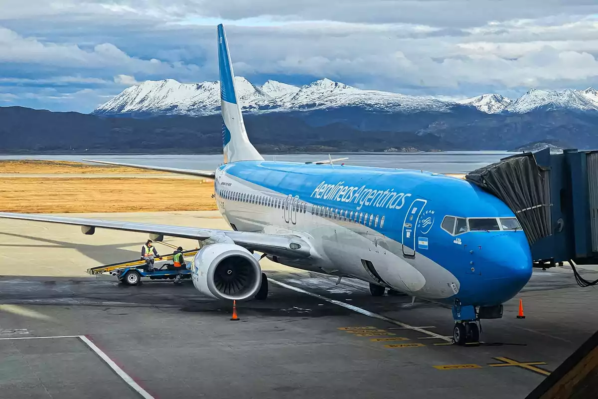 Un avión de Aerolíneas Argentinas estacionado en el aeropuerto con montañas nevadas al fondo.