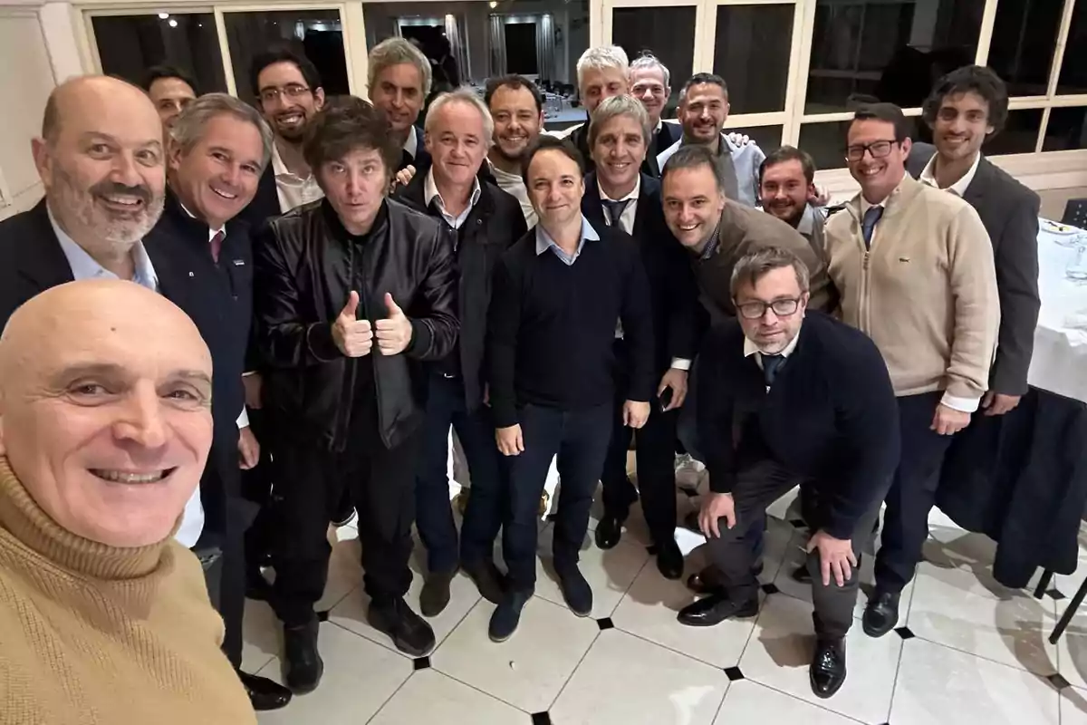 Un grupo de hombres sonrientes posando para una foto en un interior con ventanas al fondo.