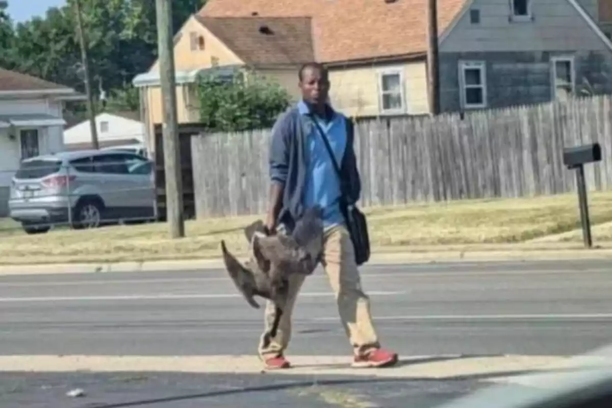 Un hombre camina por la calle llevando un ganso en la mano.