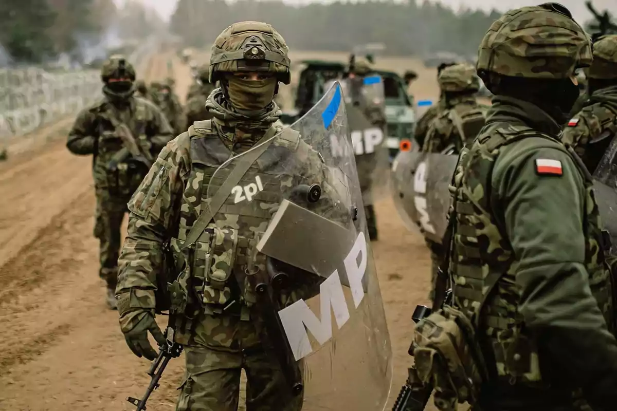 Soldados con equipo de camuflaje y escudos en un entorno al aire libre.