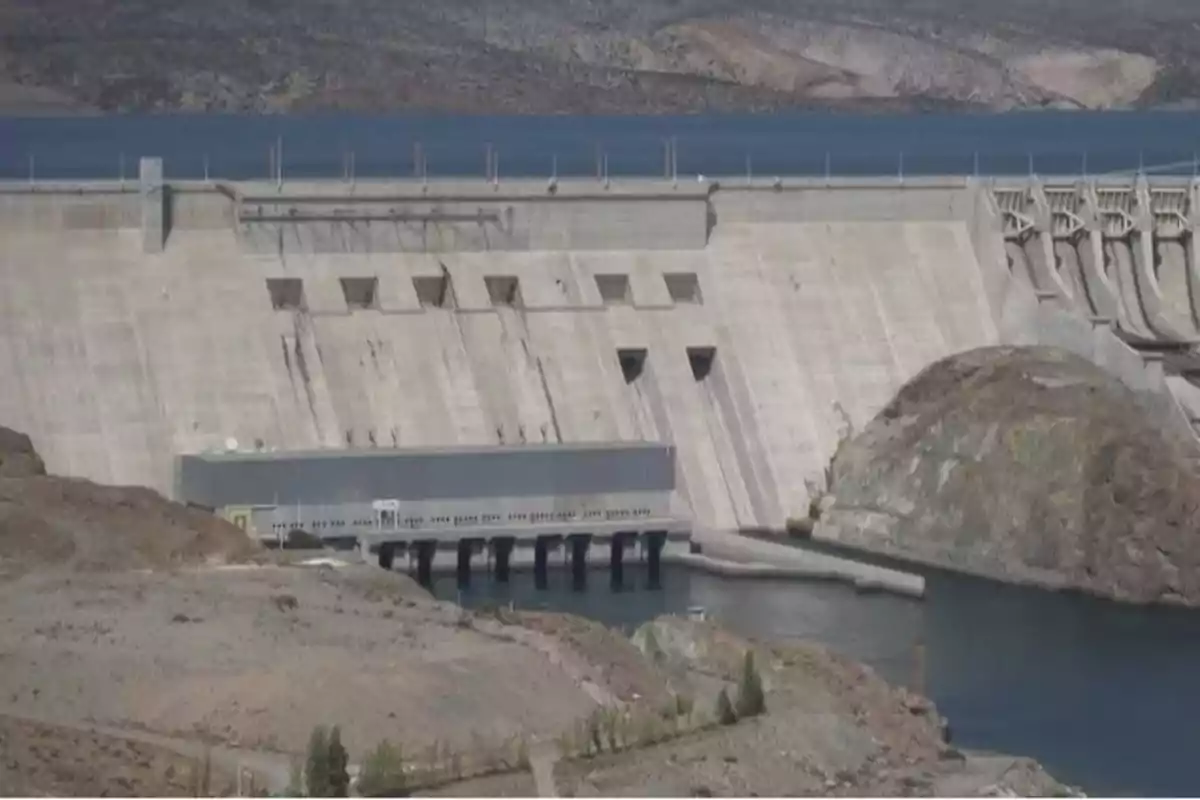 Una gran presa de concreto con agua en la parte inferior y montañas en el fondo.