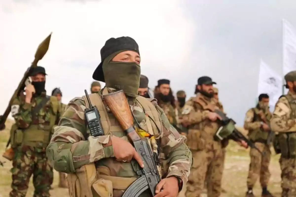 Un grupo de personas vestidas con uniformes militares y pasamontañas sosteniendo armas en un entorno al aire libre.