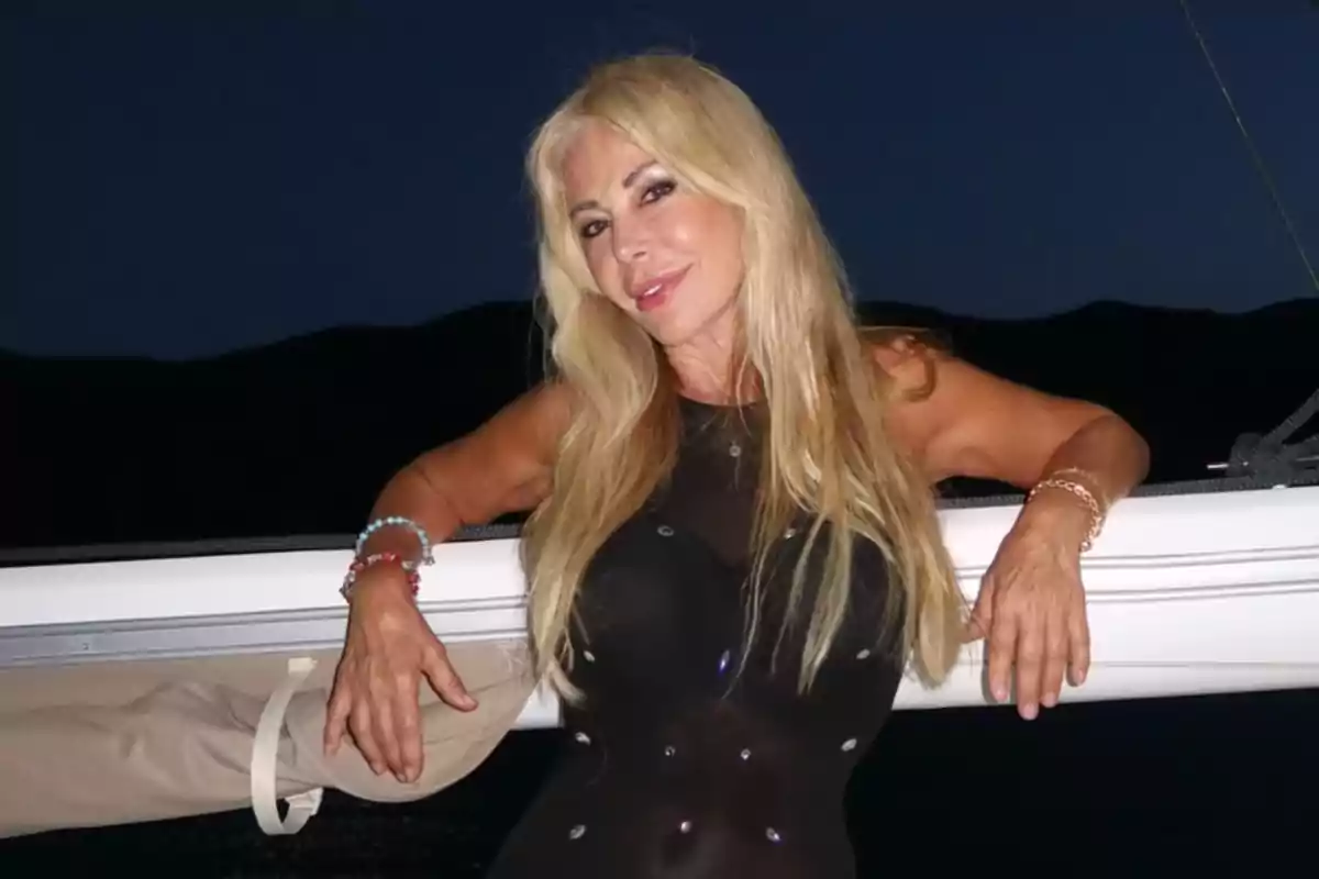 Una mujer rubia con vestido negro posando en un barco durante la noche.