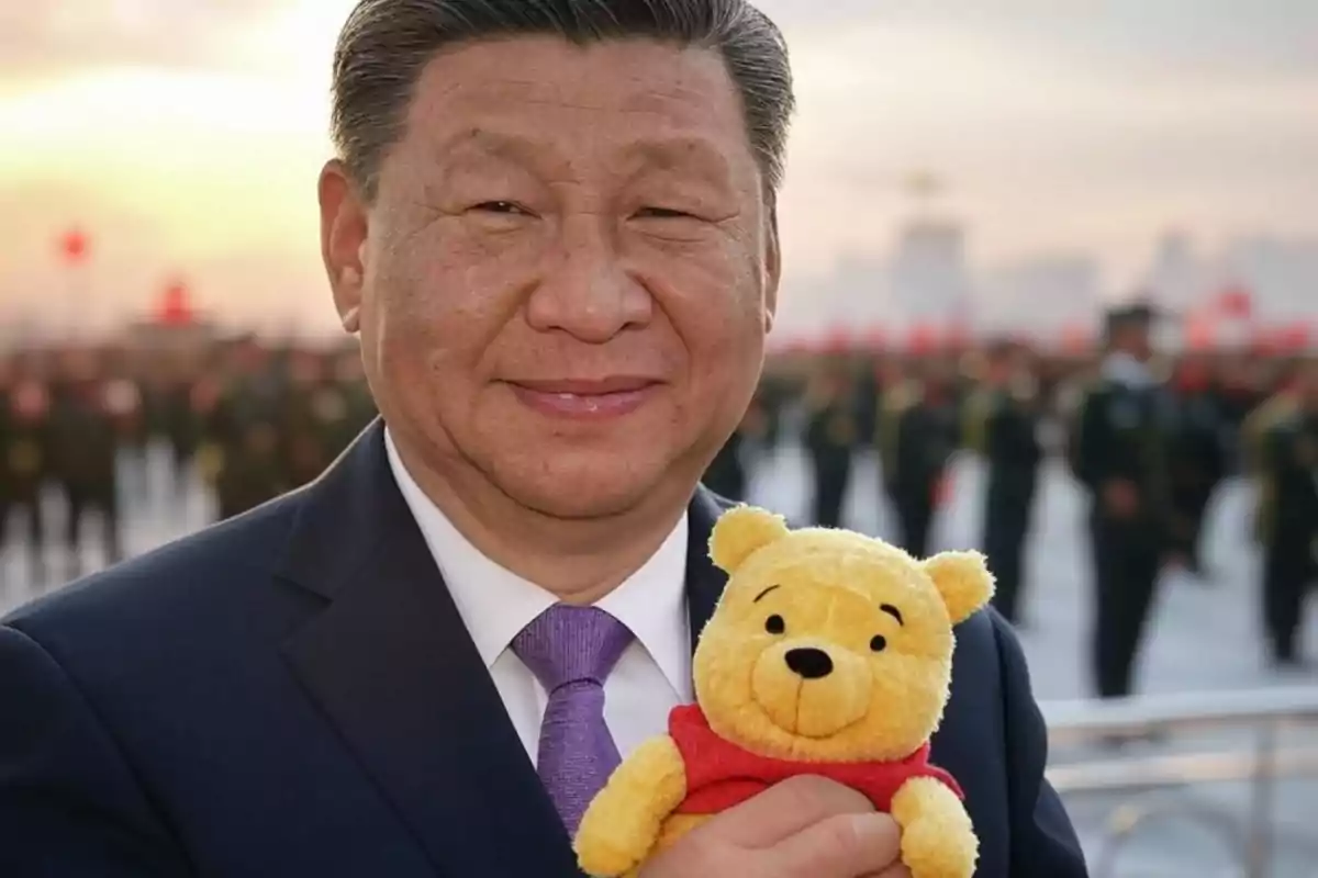 Un hombre con traje oscuro y corbata morada sostiene un peluche de Winnie the Pooh frente a un fondo de personas uniformadas y un cielo al atardecer.