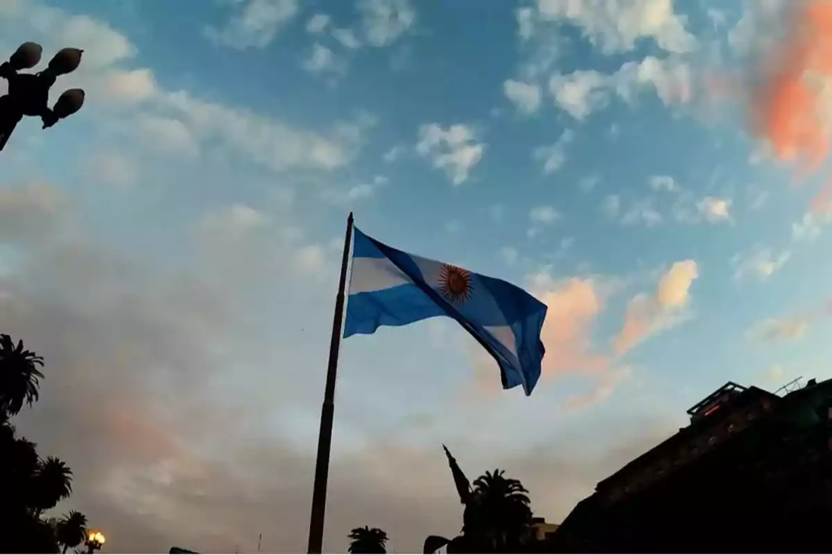 Bandera de Argentina ondeando al atardecer con un cielo parcialmente nublado.