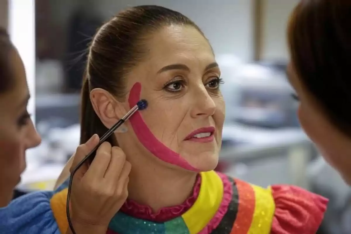 A person is being made up with a pink line on their cheek while wearing a colorful costume.