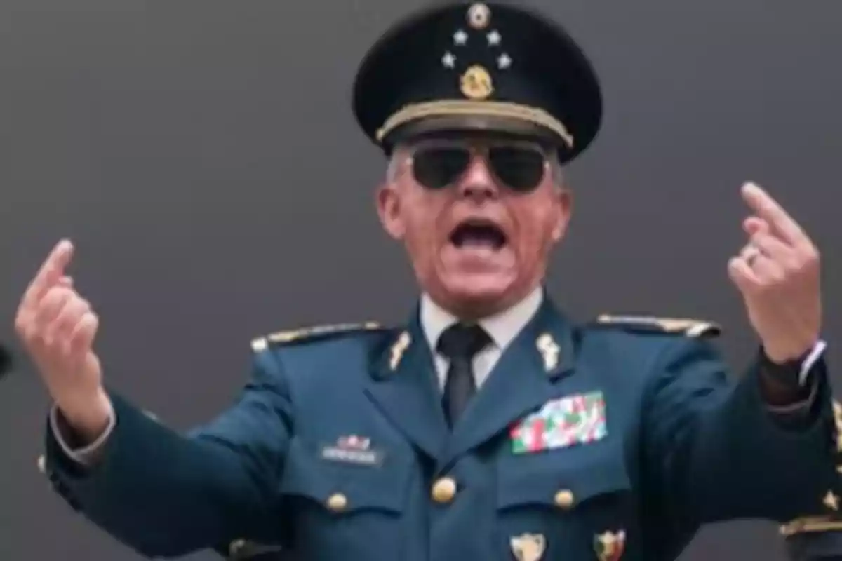 A man in a military uniform and sunglasses makes a gesture with his hands.