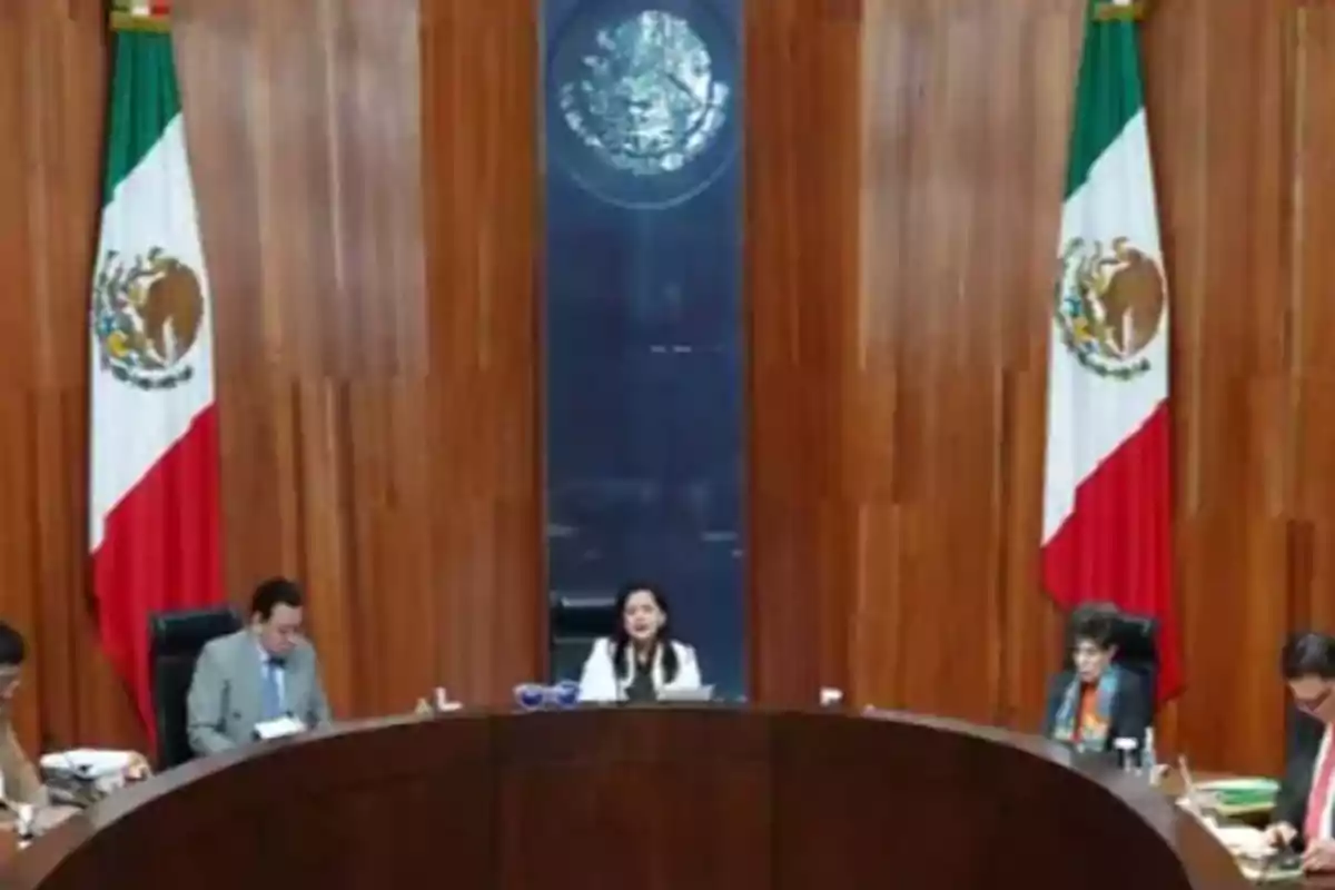 A conference room with Mexican flags and people seated at a semicircular table.