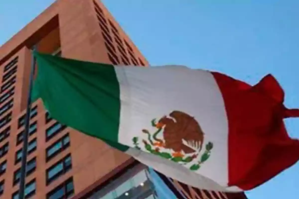 Mexican flag waving in front of a tall building under a clear sky.