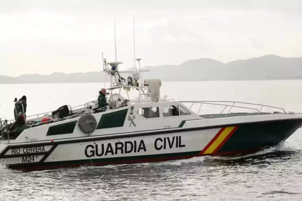 Una lancha de la Guardia Civil navegando en el agua con montañas al fondo.