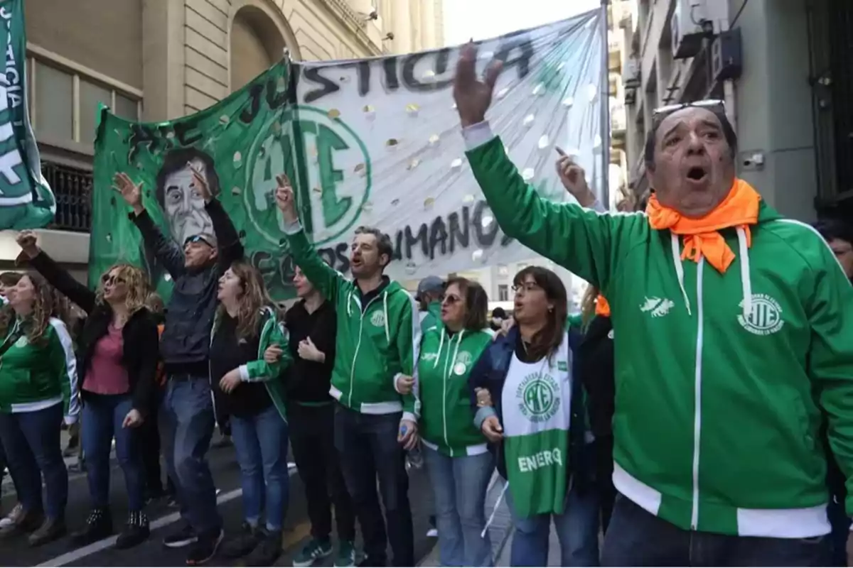 Un grupo de personas vestidas con chaquetas verdes participa en una manifestación en la calle sosteniendo pancartas y banderas.