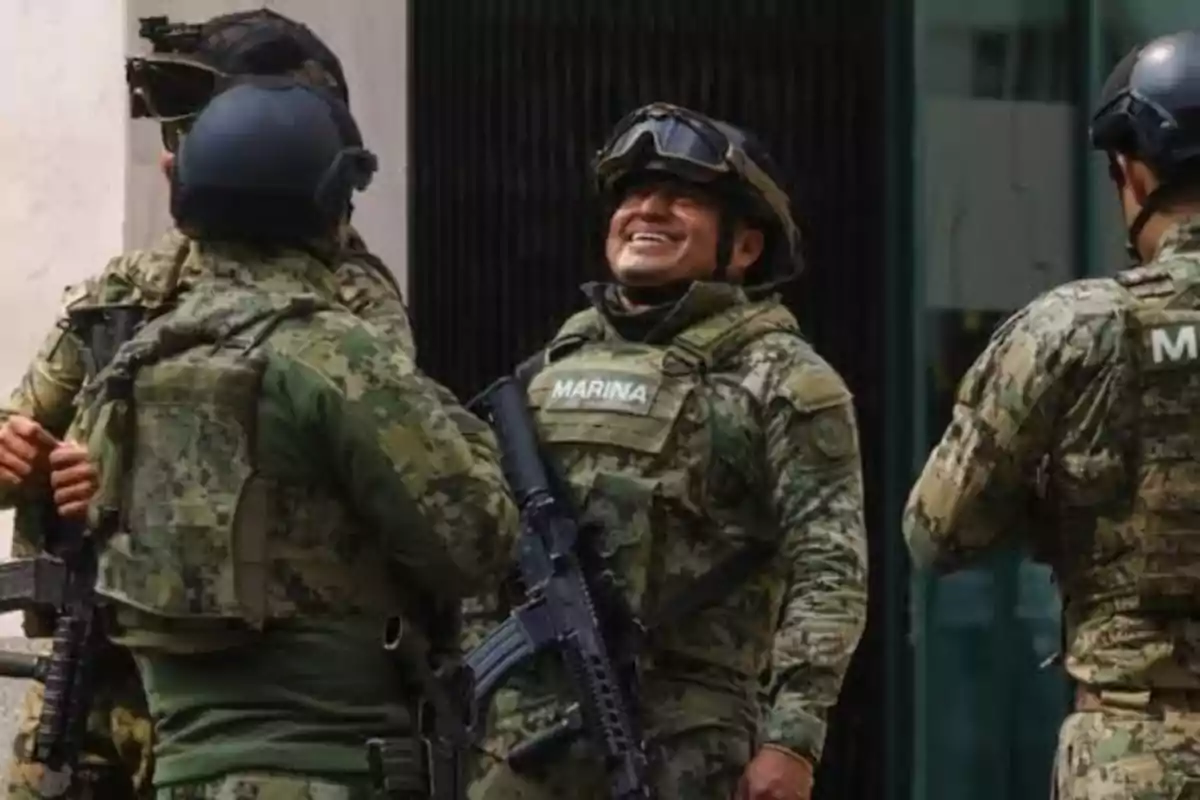 A group of navy soldiers dressed in camouflage uniforms and helmets, one of them smiling.