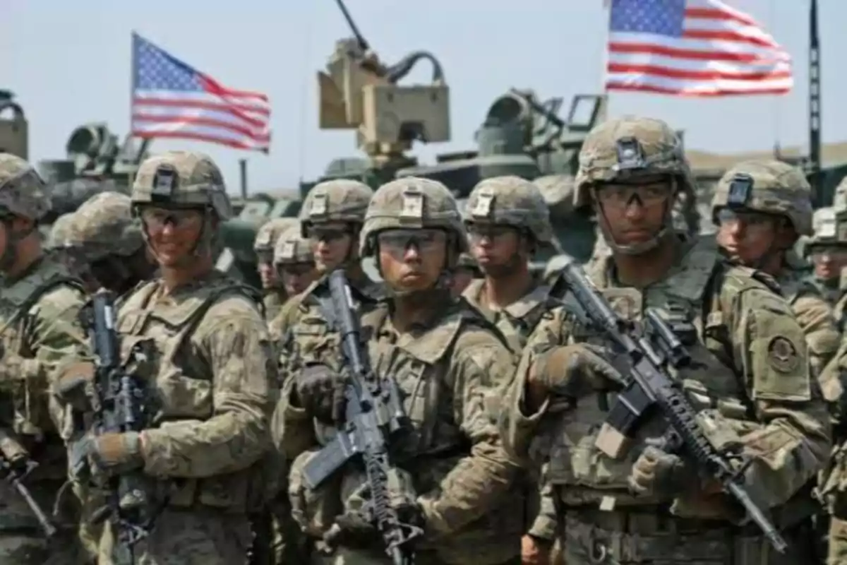 Soldiers in military uniform holding rifles with United States flags waving in the background.