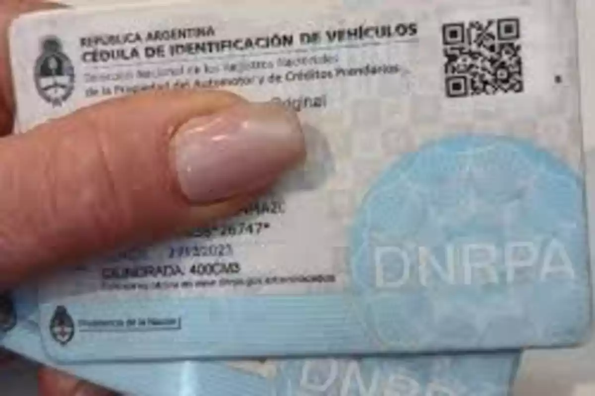 Una mano sostiene una cédula de identificación de vehículos de la República Argentina con un diseño en tonos azules y un código QR visible.