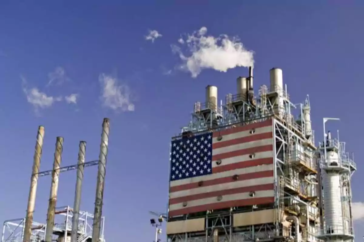 Industrial plant with chimneys and a large United States flag on the structure under a blue sky.