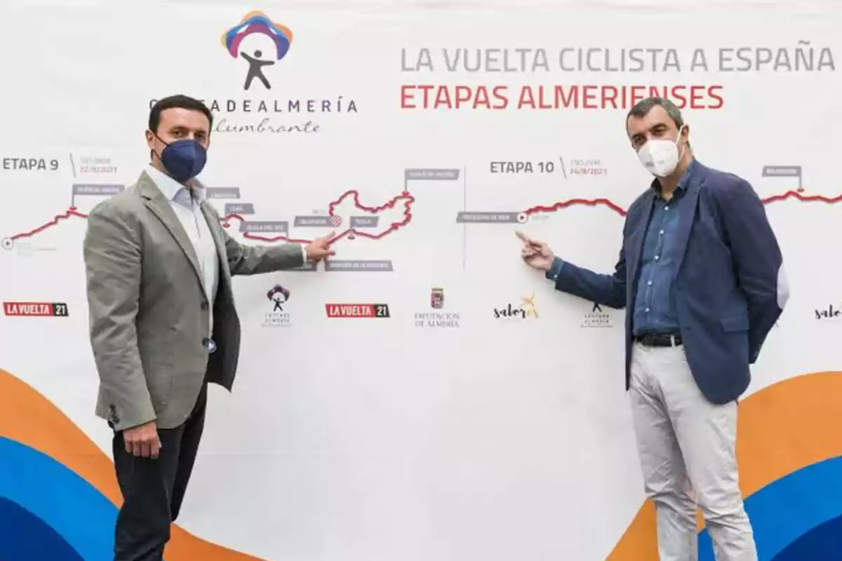 Dos personas con mascarillas señalan un mapa de las etapas almerienses de la Vuelta Ciclista a España.