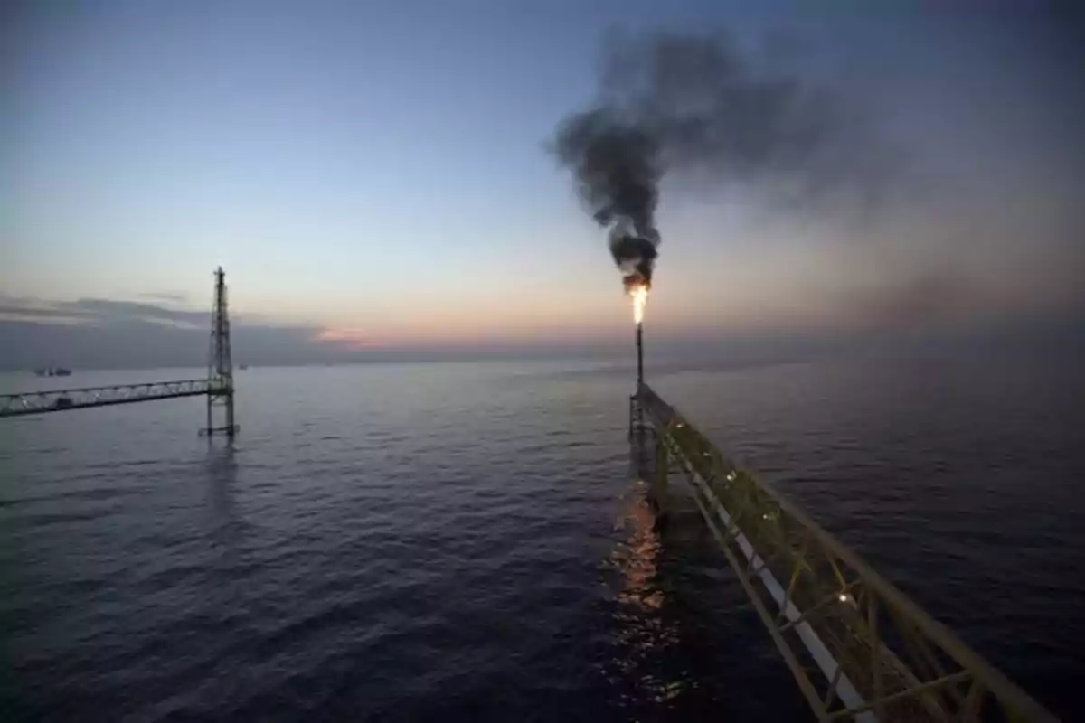 Offshore oil platform with a lit flare at sunset.