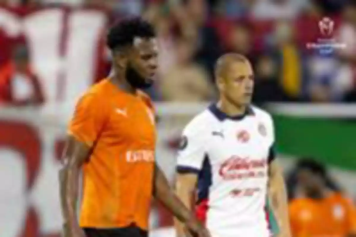 Two players on the field, one in an orange uniform and the other in a white uniform, during a match.