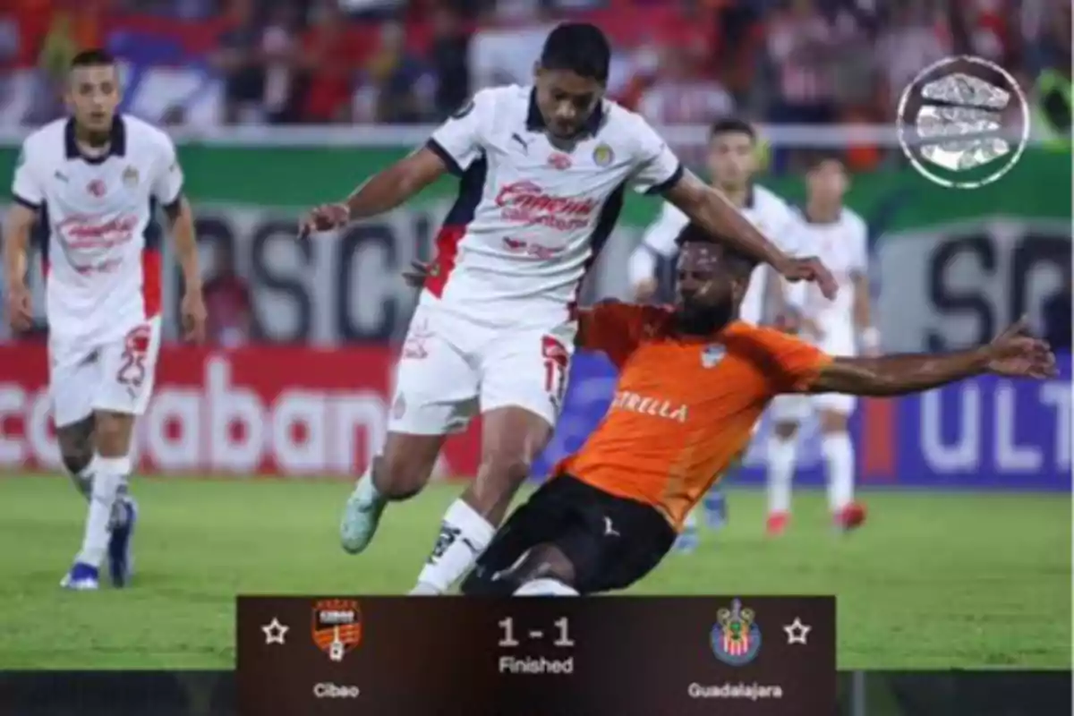 A player in a white uniform tries to advance while another player in an orange uniform slides to take the ball away in a match that ended 1-1 between Cibao and Guadalajara.