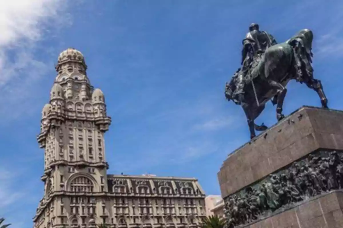 Edificio histórico y estatua ecuestre en una plaza bajo un cielo azul.