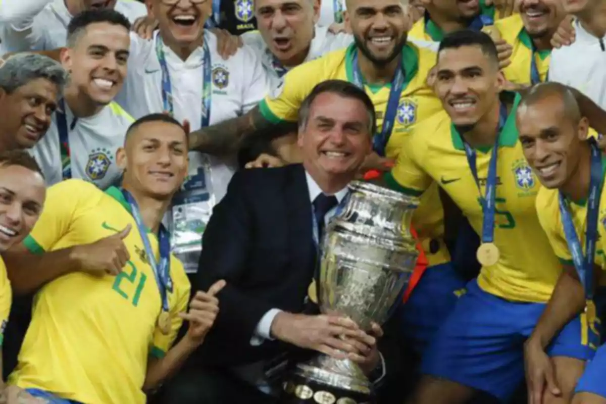 Un grupo de personas sonrientes con camisetas amarillas celebrando con un trofeo grande.