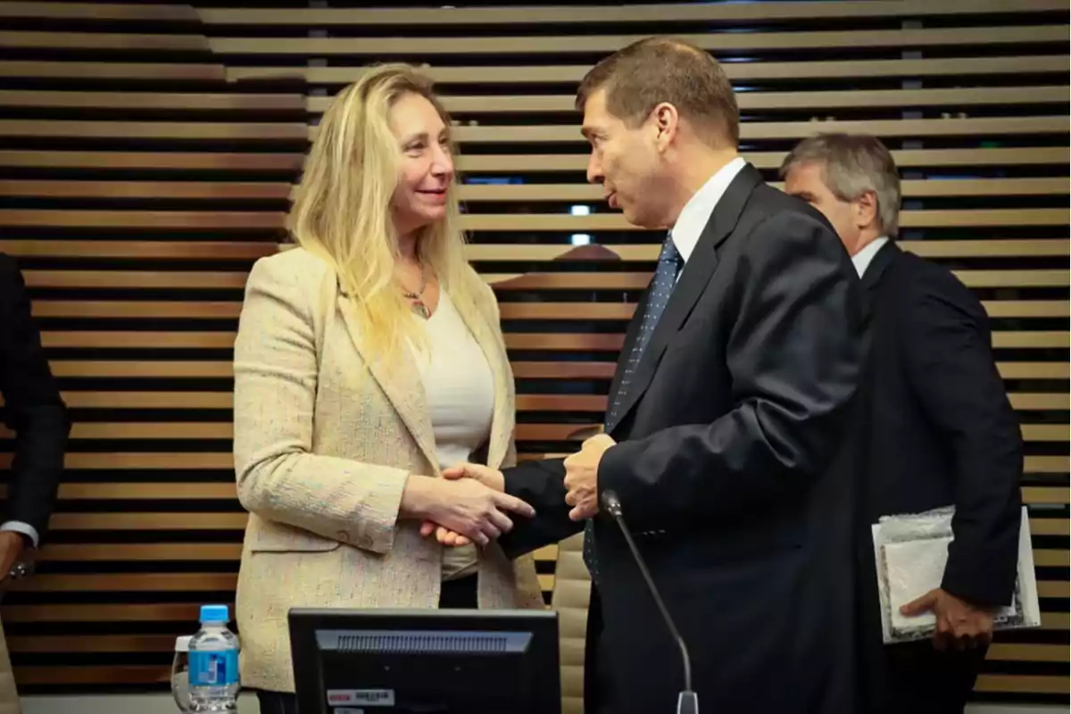 Dos personas se dan la mano en un entorno profesional con fondo de listones de madera.