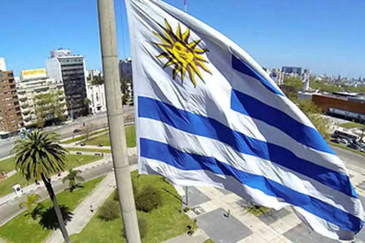 Bandera de Uruguay ondeando en un entorno urbano con cielo despejado.