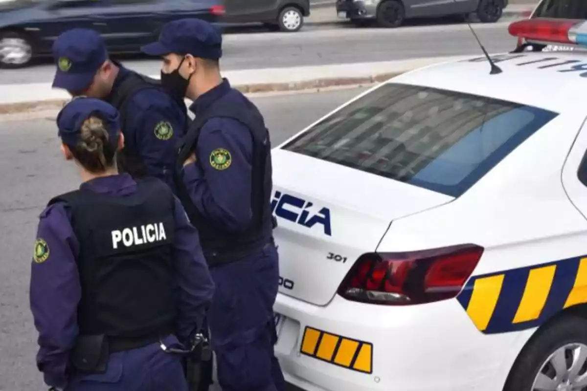 Policías de pie junto a un coche patrulla en una calle.