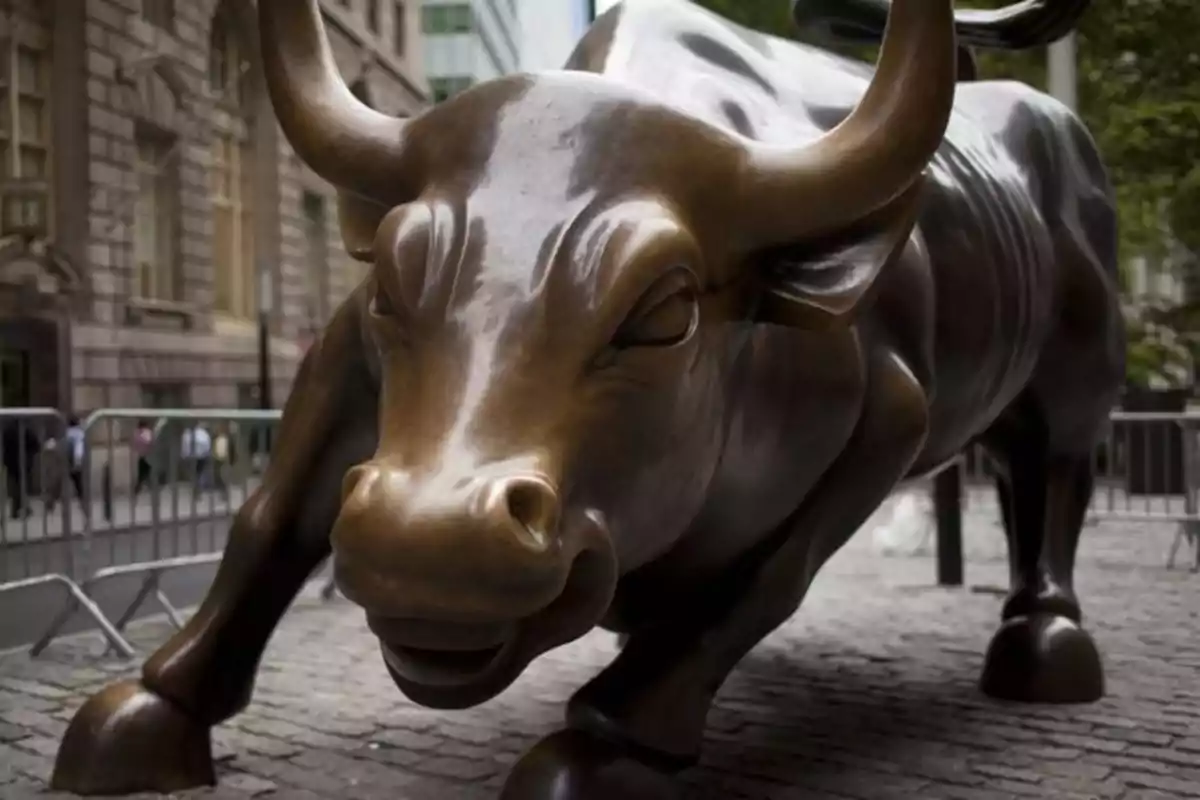 Escultura de un toro de bronce en una calle rodeada de edificios y barreras metálicas.