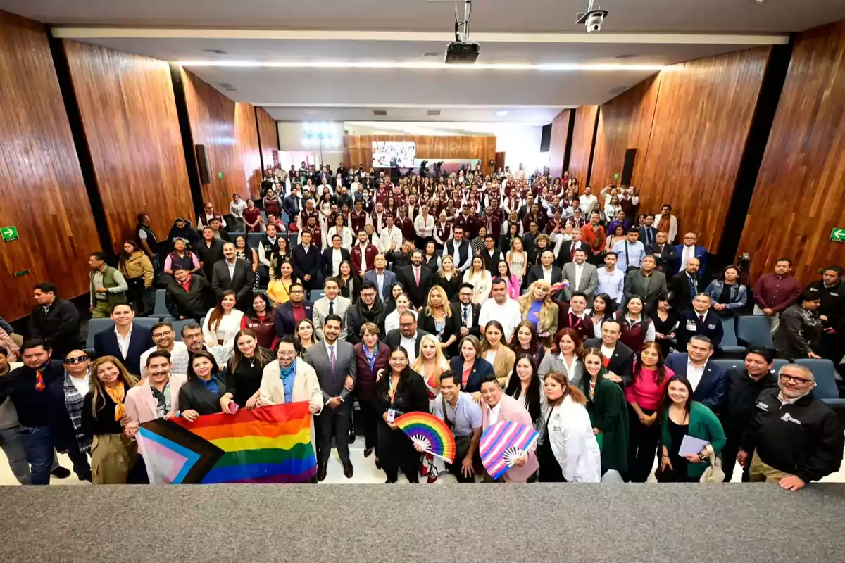 A large group of people posing in an auditorium, some holding flags and fans with rainbow colors.