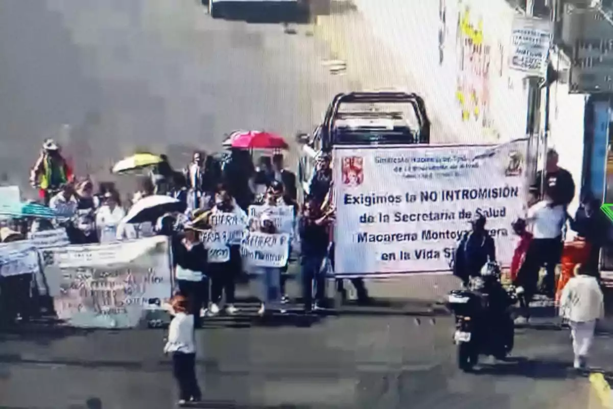 Un grupo de personas participa en una manifestación en la calle, sosteniendo pancartas y carteles con mensajes de protesta.