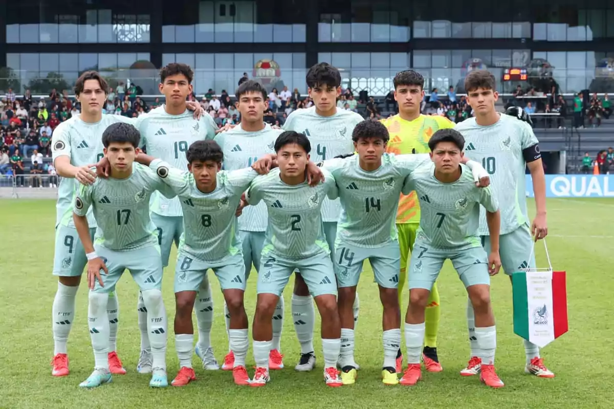 A youth soccer team poses for a group photo on the field before a match, with players wearing green uniforms and a stadium full of spectators in the background.