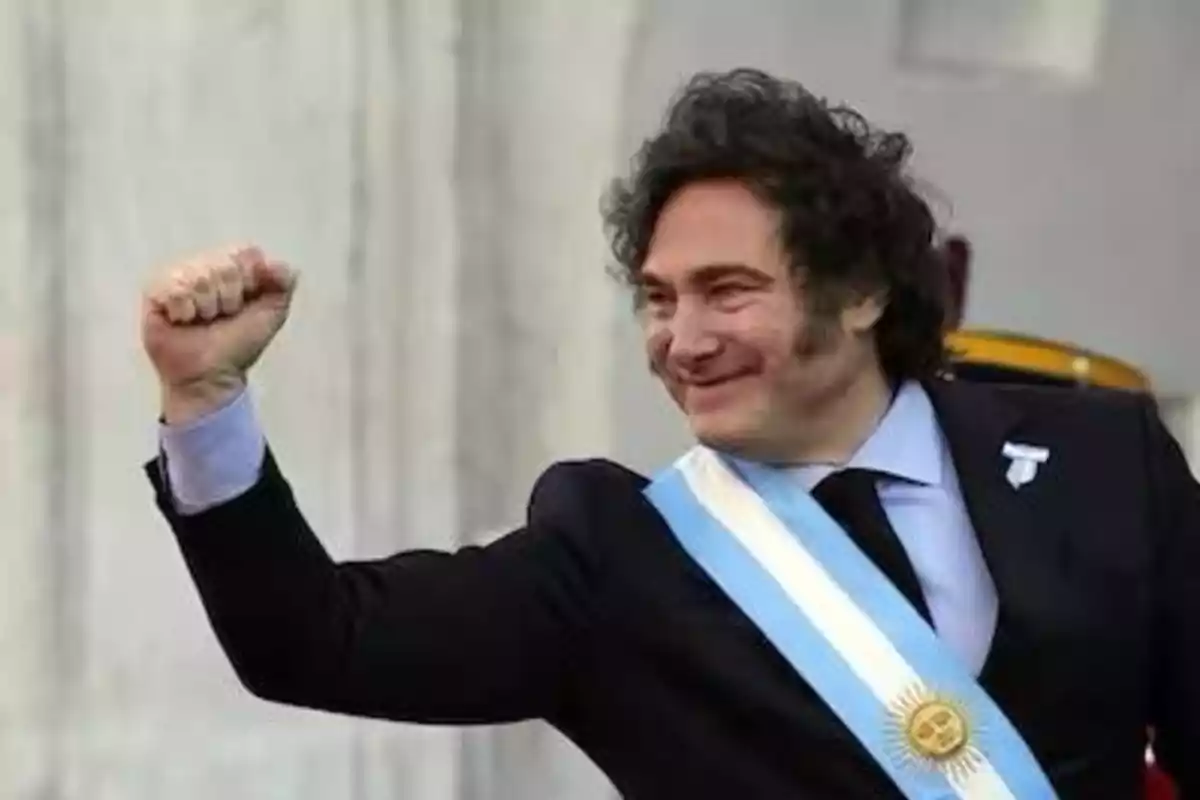 Hombre con traje y banda presidencial levantando el puño en señal de celebración.