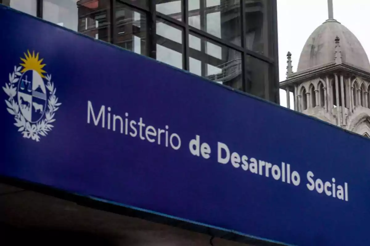 Un cartel azul del Ministerio de Desarrollo Social con un edificio antiguo al fondo.