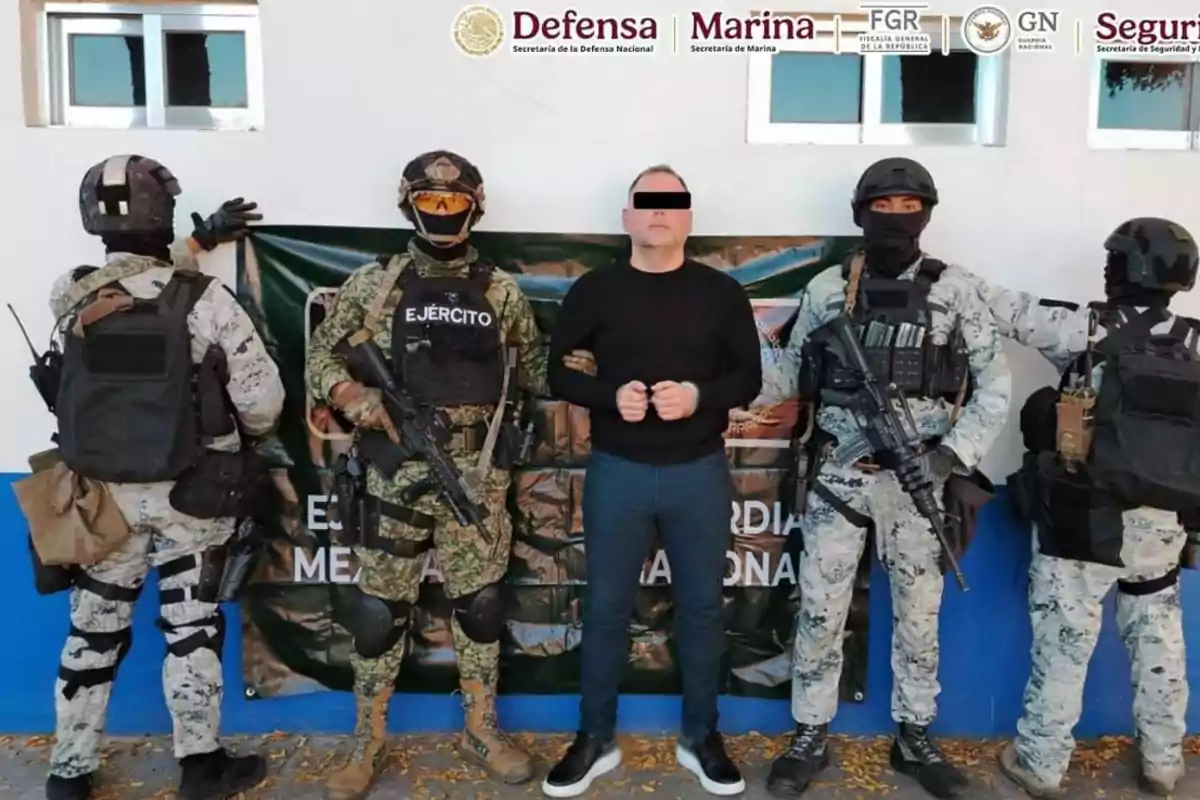 Un grupo de militares armados escolta a un hombre con los ojos cubiertos frente a un cartel institucional.