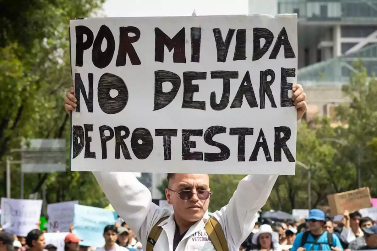 Persona sosteniendo un cartel que dice "Por mi vida no dejaré de protestar" en una manifestación.