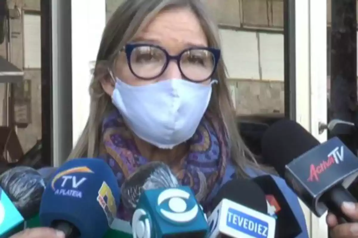 A woman wearing a mask and glasses is being interviewed by several media outlets.