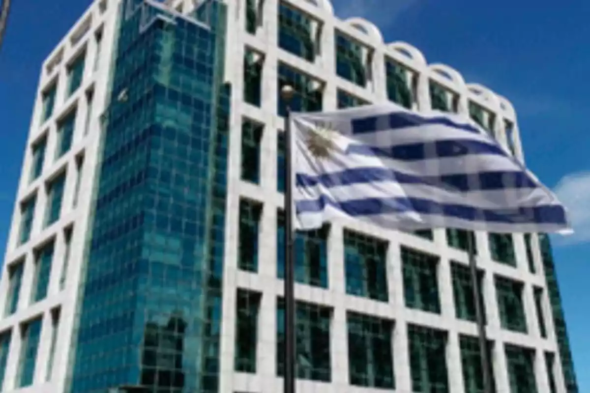 Edificio moderno con fachada de vidrio y bandera de Uruguay ondeando en primer plano.