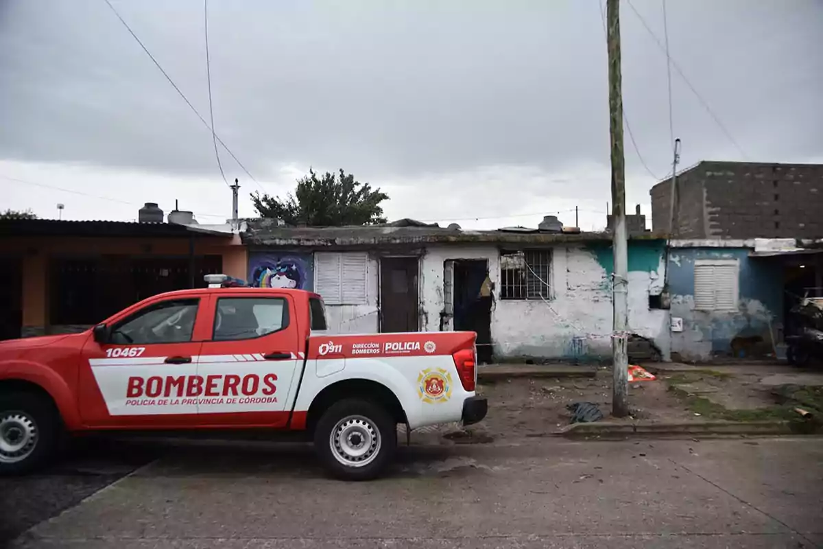 Una camioneta de bomberos de la provincia de Córdoba estacionada frente a una casa deteriorada en un día nublado.