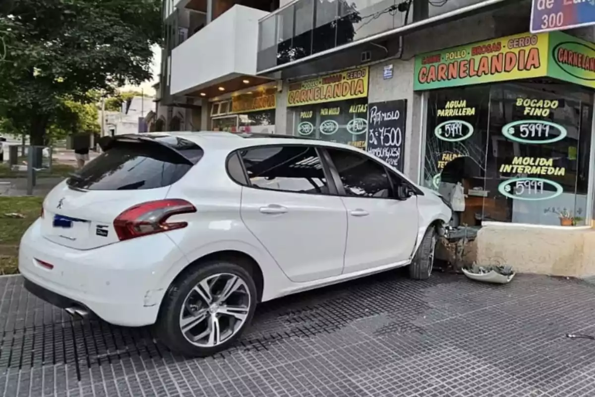 Un coche blanco se ha estrellado contra la fachada de una tienda llamada "Carnelandia" en una calle urbana.